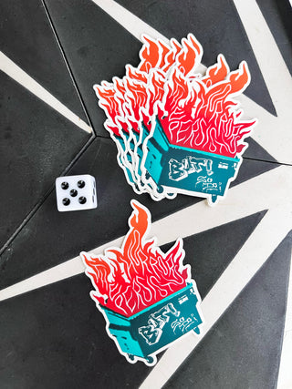 Dumpster fire stickers that say "the horrors persist but so do I" on a black tile background